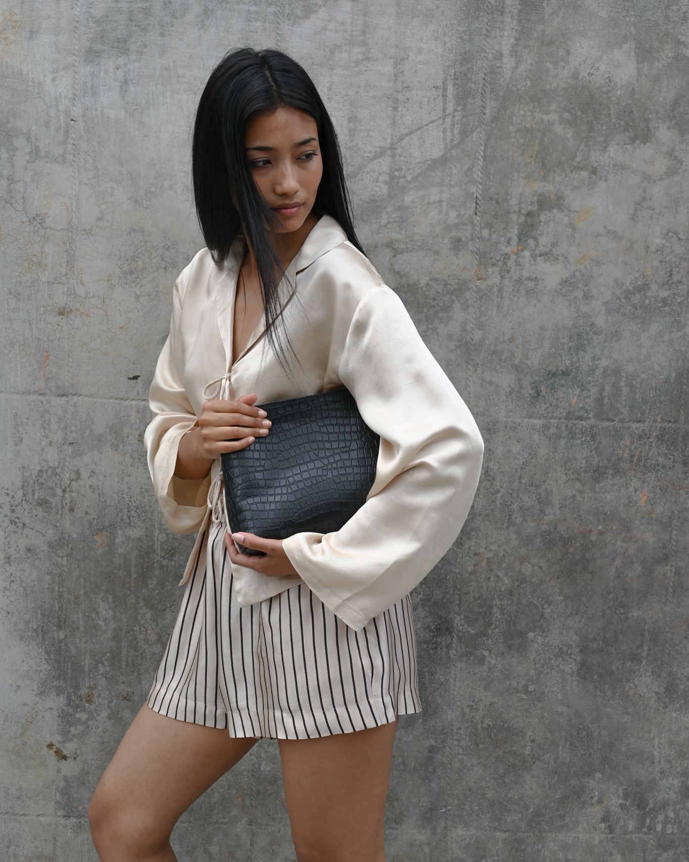 Woman holding a clutch against a gray concrete wall