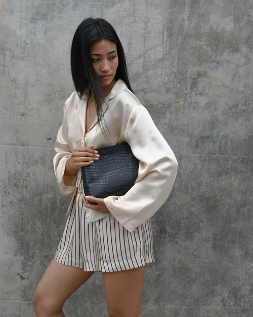 Woman holding a clutch against a gray concrete wall